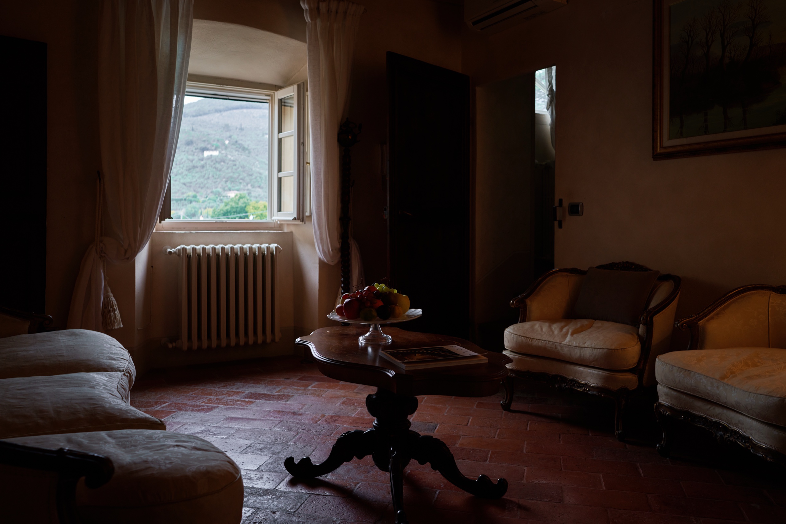 Salotto in penombra di Villa Scorzi con poltrone e divani di gusto classico e pavimento in cotto
